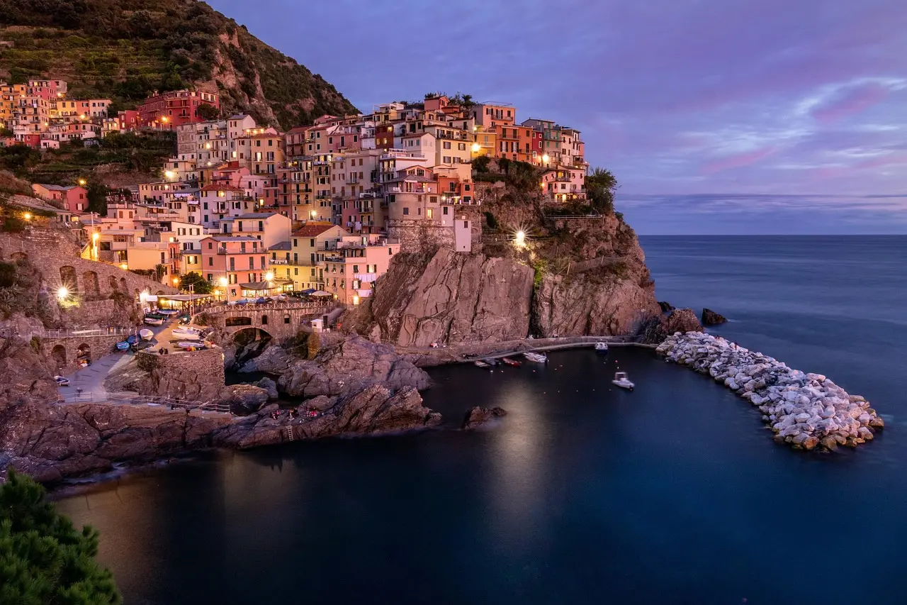 Twilight in Manarola, Cinque Terre — glowing harbor lights and pastel homes define this beloved coastal gem among must-visit places in Italy Manarola village at twilight with colorful buildings stacked along rocky coastline and harbor lights reflecting on water