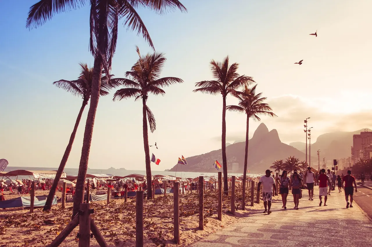 Golden-hour sunset over Copacabana Beach in Rio de Janeiro, Brazil — palm-fringed shoreline, striped umbrellas, and Atlantic waves reflecting vibrant coastal energy Sunset over Copacabana Beach with colorful umbrellas and ocean waves