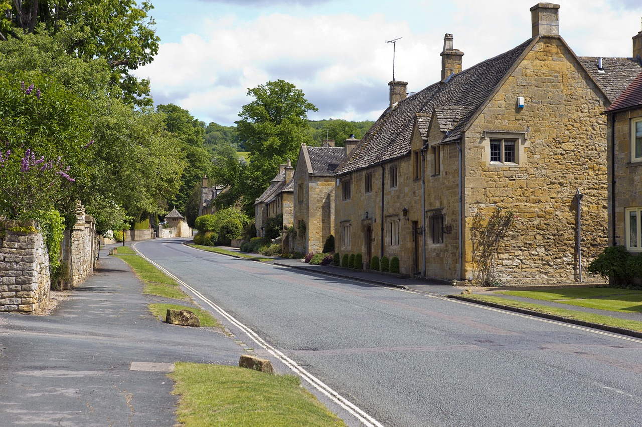 Storybook perfection in a Cotswolds village — a beloved, timeless highlight among must-visit places in the UK Quaint honey-stone village with flower-lined street and stone bridge over a gentle river