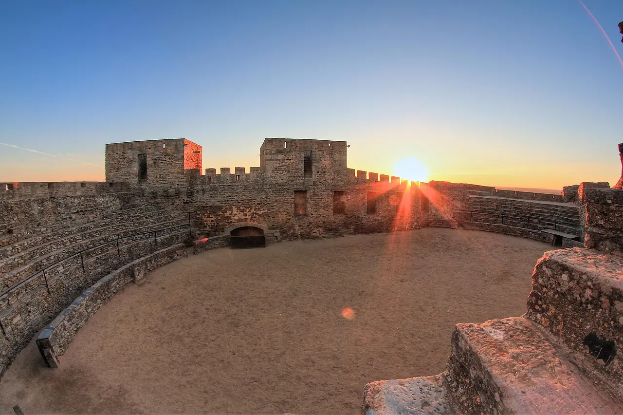 Sunset over medieval Monsaraz, highlighting its granite castle silhouette and whitewashed homes against the vast, golden Alentejo plains Panoramic view of Monsaraz village at sunset with castle ruins and golden plains stretching to the horizon