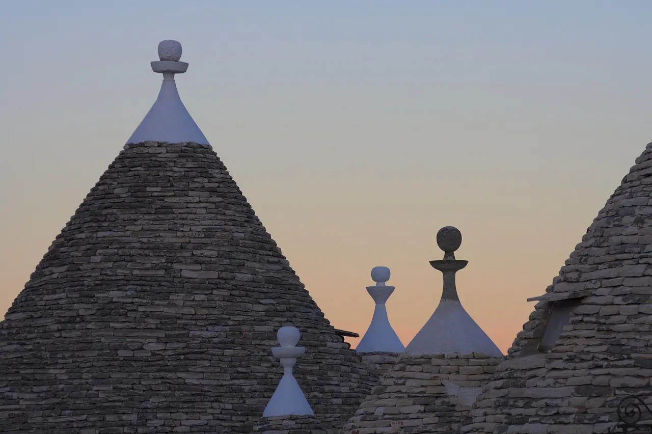 Iconic conical trulli houses in Alberobello, Puglia — whimsical, historic, and utterly unique among must-visit places in Italy Alberobello’s trulli district at midday with conical limestone roofs and flowering bougainvillea