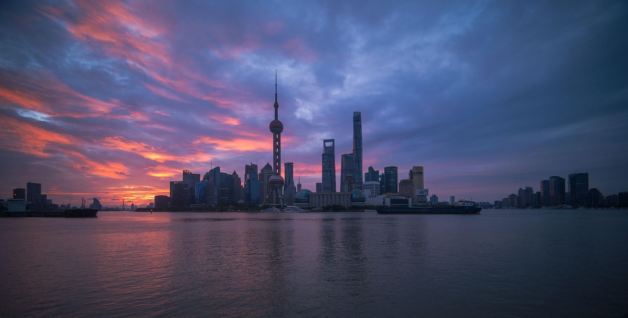 Golden-hour view of the Shanghai Bund featuring neoclassical buildings on one bank and glittering Pudong towers across the Huangpu River Shanghai Bund at dusk with historic buildings on left and illuminated Pudong skyscrapers on right across Huangpu River