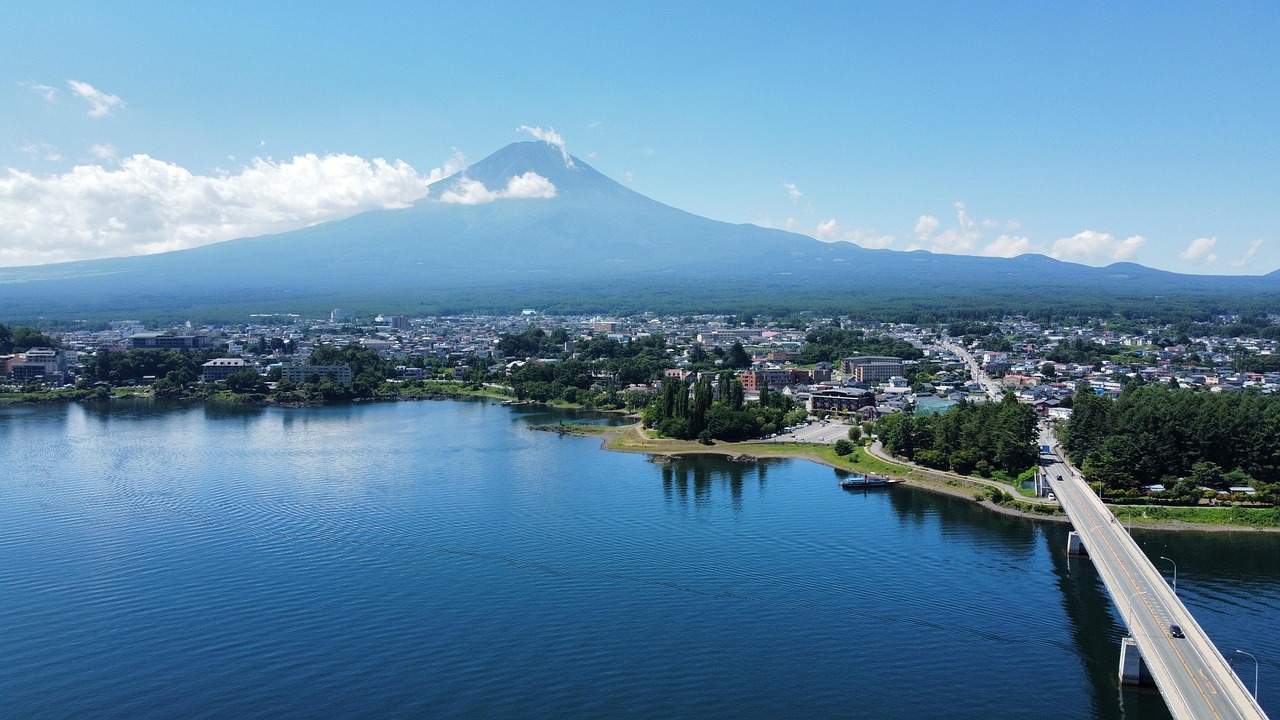 Sunrise over Mount Fuji reflected in Lake Kawaguchi, surrounded by spring cherry blossoms — one of Japan's most iconic scenic views Panoramic view of Mount Fuji reflected in Lake Kawaguchi at sunrise, with cherry blossoms framing the shore