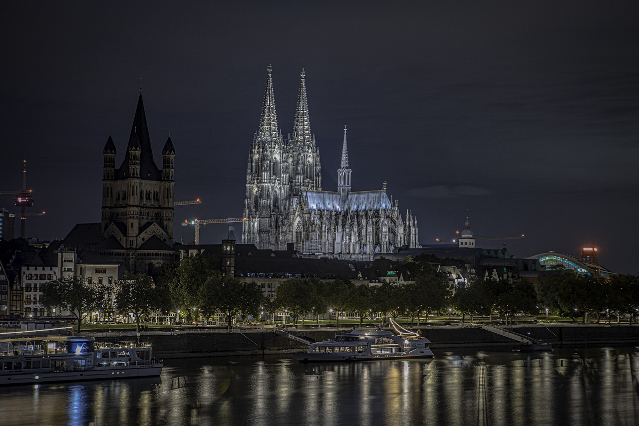 Cologne Cathedral reflected in the Rhine at midday, with passenger riverboats gliding past — a spiritual and architectural highlight among the 15 must-visit places in Germany. Cologne Cathedral towering over the Rhine River with river cruise boats passing below