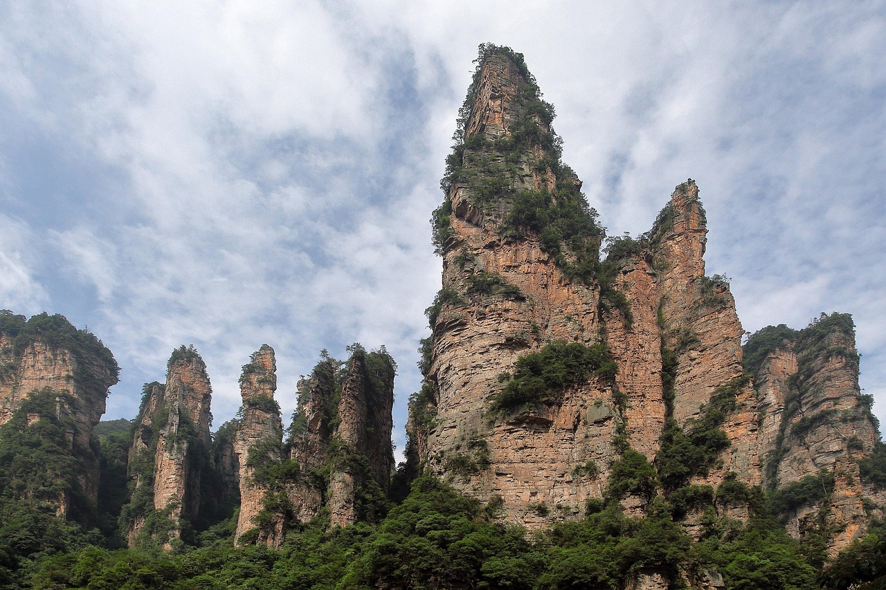 Misty morning in Zhangjiajie National Forest Park reveals surreal quartzite spires draped in emerald moss and veiled in soft cloud Towering quartzite sandstone pillars covered in green moss and mist in Zhangjiajie National Forest Park