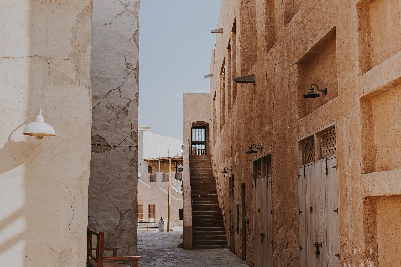 Sun-dappled cobblestone alley in Dubai’s Al Fahidi Historical Neighbourhood showcasing historic coral-stone buildings and iconic barjeel (wind towers) Traditional wind-tower architecture and arched alleyways in Al Fahidi Historical District