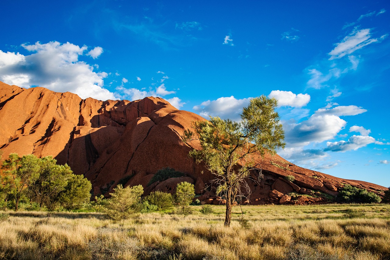 Uluru rising majestically at first light, its surface radiating deep crimson tones across the silent Central Australian desert — a spiritual and geological icon Uluru at sunrise with deep red hues and desert landscape
