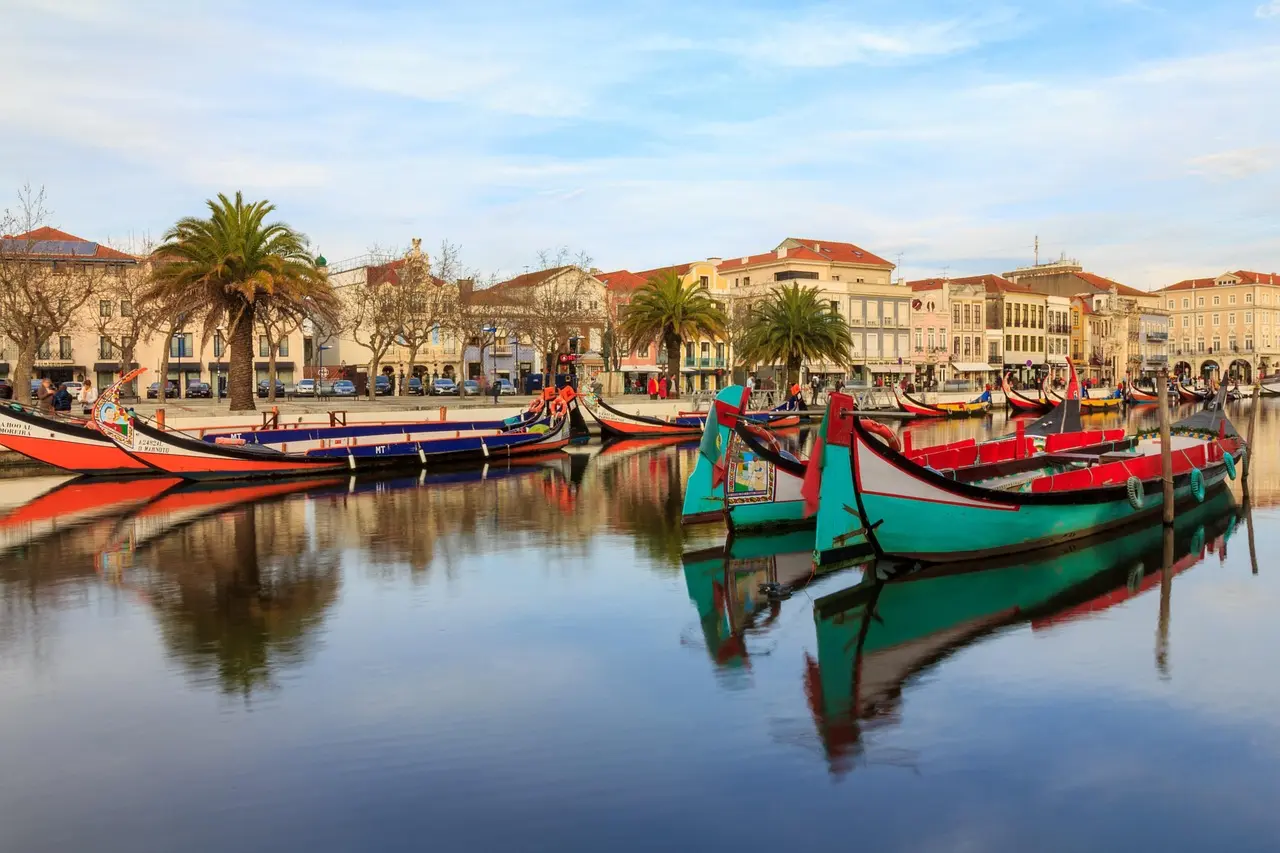 Brightly painted moliceiro boat floating along Aveiro’s central canal, flanked by ornate early-20th-century facades and hanging flower baskets Traditional moliceiro boat gliding through Aveiro’s main canal lined with colorful Art Nouveau buildings