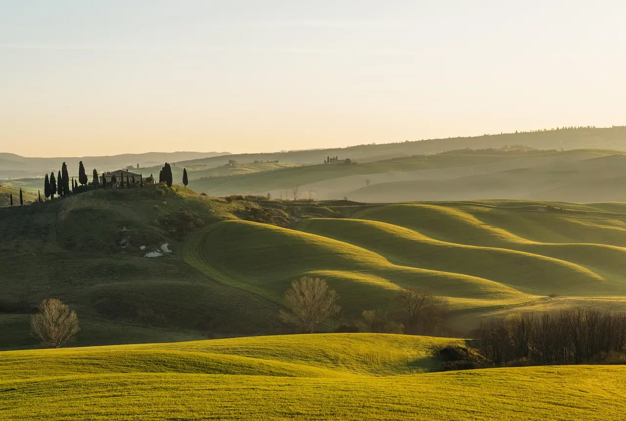 Golden sunrise over vineyard-draped Tuscan hills — serene, iconic, and essential among must-visit places in Italy Sunrise over rolling Tuscan hills with cypress trees, vineyards, and a stone farmhouse