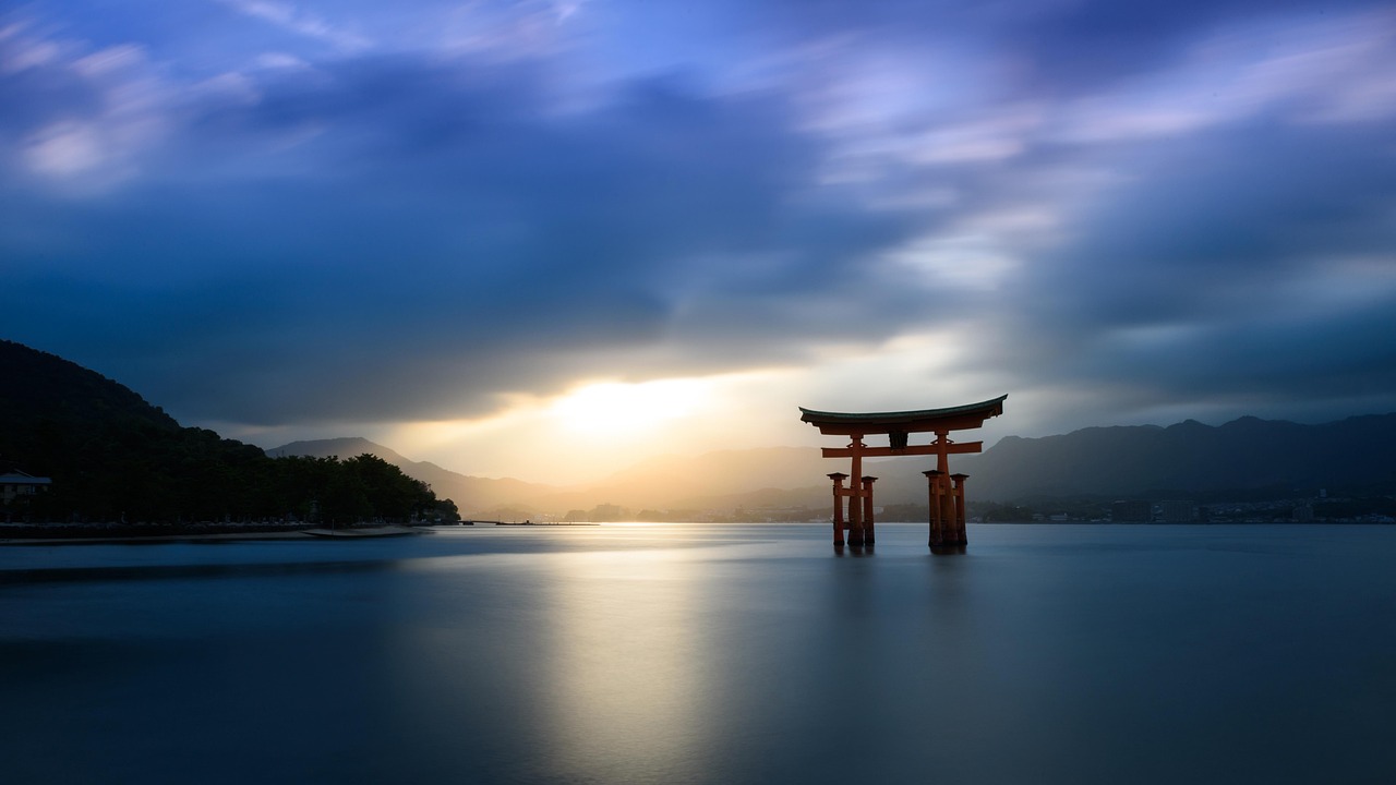 Golden-hour reflection of Itsukushima Shrine’s torii gate on Miyajima Island — a serene, iconic scene among the most spiritual places to visit in Japan Sunset over Miyajima Island with Itsukushima Shrine, torii gate, and calm water reflecting orange sky