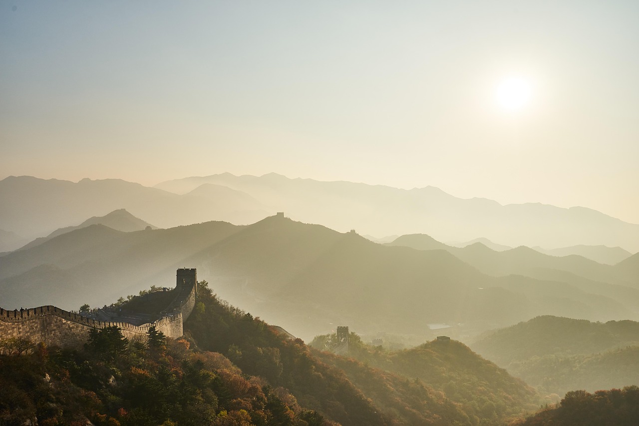 Early morning light illuminates the historic Mutianyu section of the Great Wall of China, surrounded by forested hills and soft morning mist Sunrise over the Great Wall of China at Mutianyu with misty mountains in the background