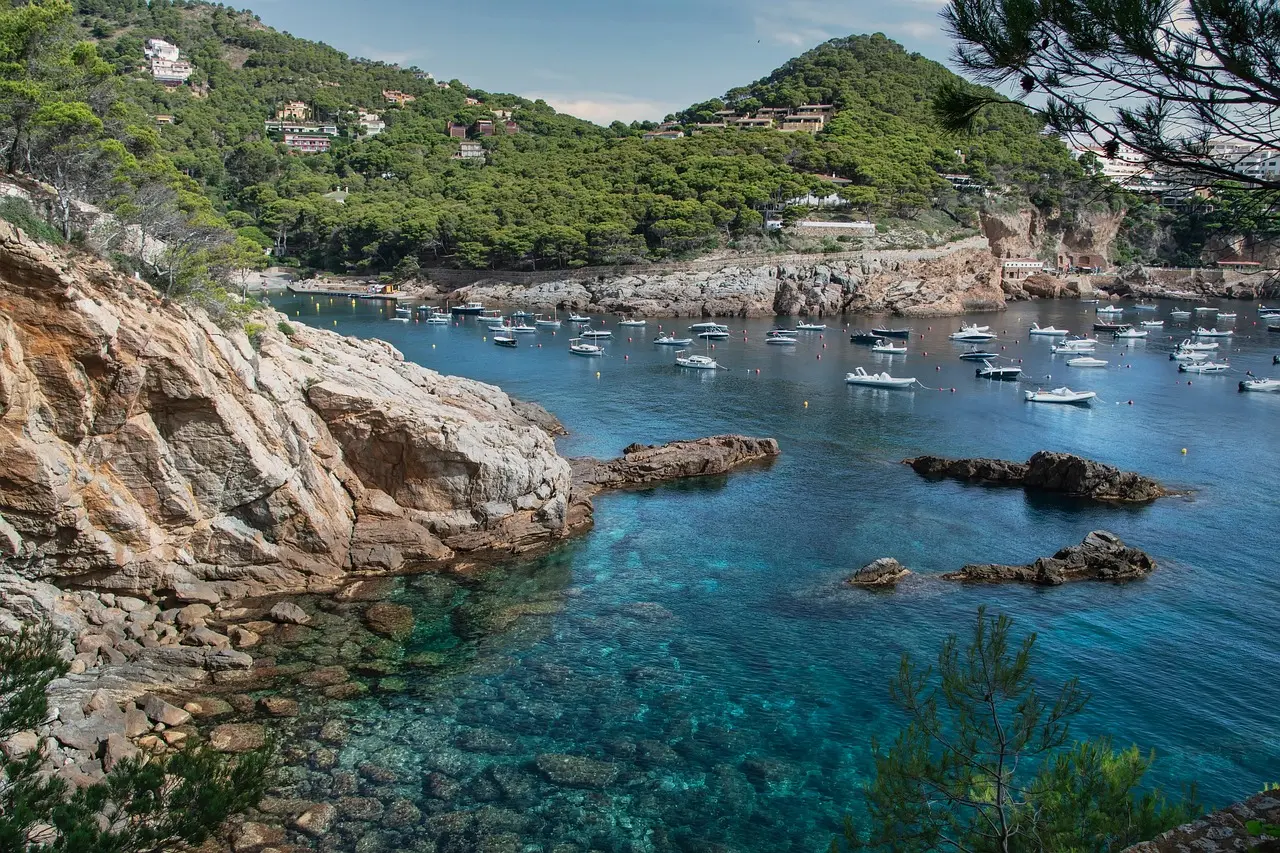 A pristine cove on Costa Brava — where rugged Mediterranean beauty meets tranquility, highlighting why this coast remains one of Spain’s most treasured must-visit places in Spain. Rocky cove with turquoise water and pine-covered cliffs on Costa Brava