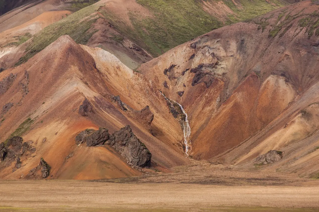 Vibrantly colored rhyolite mountains near Landmannalaugar with active geothermal steam vents and lava flows Hiker walking across colorful rhyolite mountains near Landmannalaugar with steam vents and lava fields