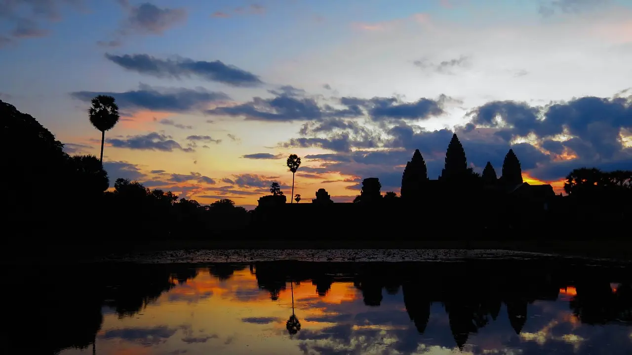 Timeless romance at dawn — a defining visual of culturally rich honeymoon destinations in Asia Silhouette of couple standing before Angkor Wat at dawn, soft light illuminating ancient stone carvings and reflecting pool