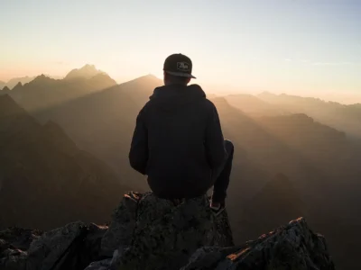 A lone hiker silhouetted against a golden alpine meadow with snow-draped peaks in the distance
