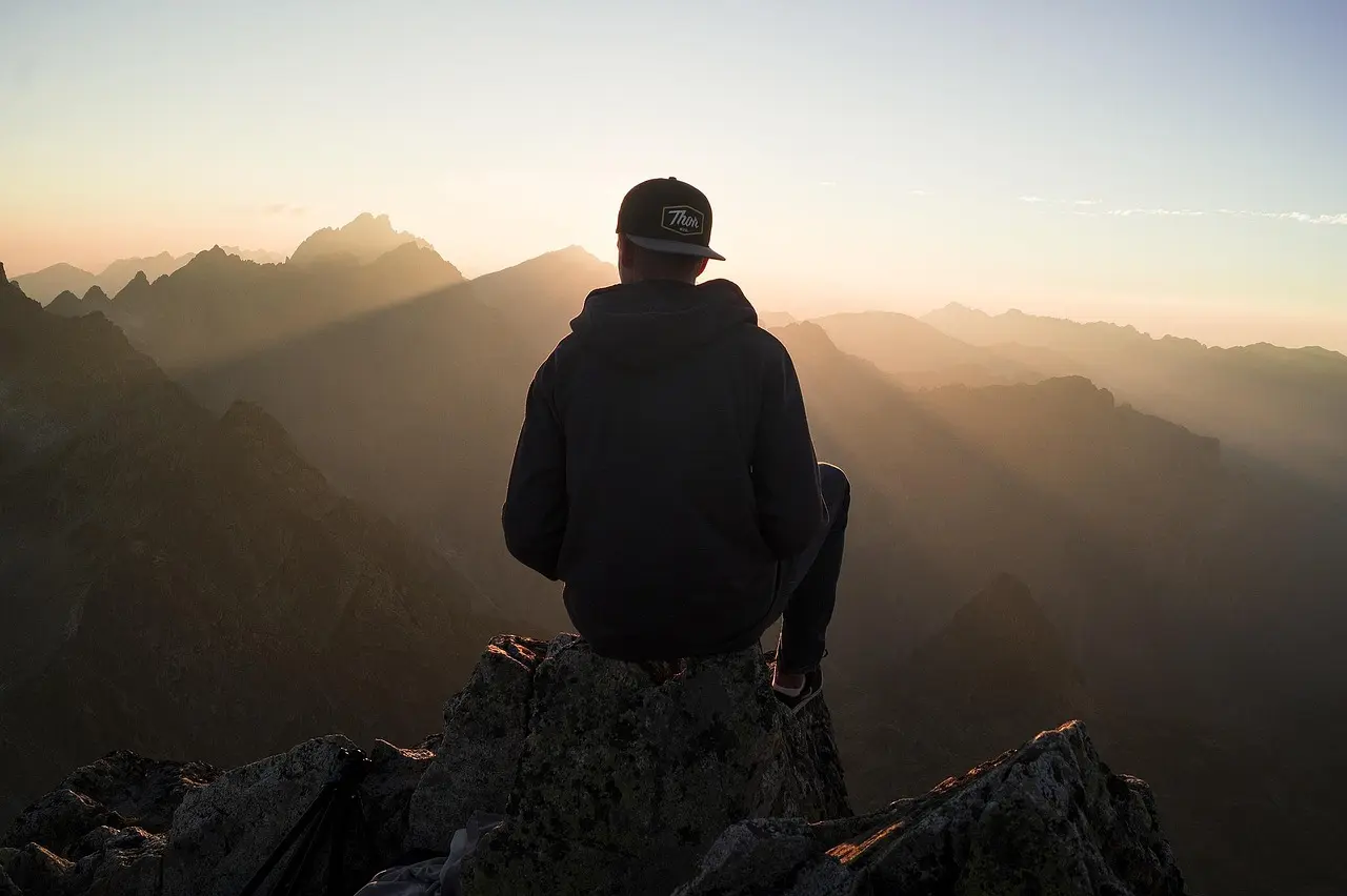 A quiet moment of reflection while appreciating natural scenery in the Swiss Alps at dawn A lone hiker silhouetted against a golden alpine meadow with snow-draped peaks in the distance