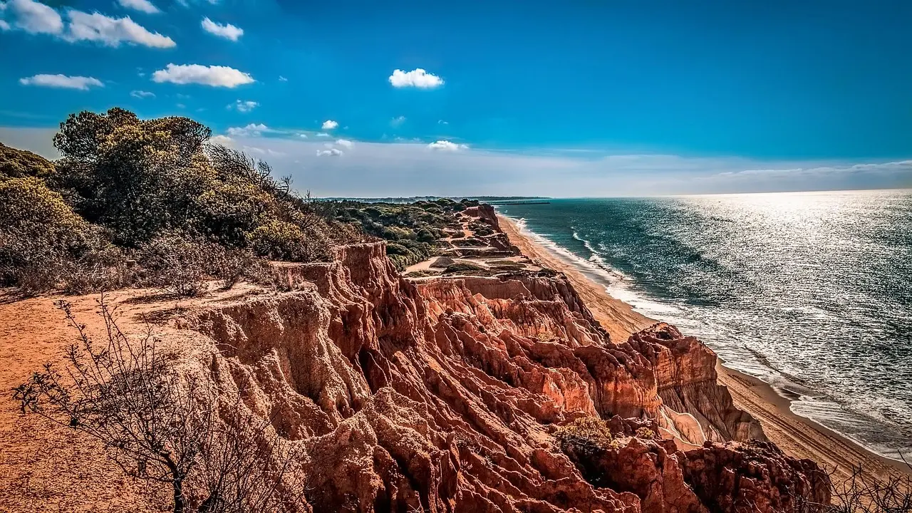 A tranquil, uncrowded stretch of the Algarve coastline—perfect for sound-based relaxation travel and circadian-aligned decompression. Secluded golden-sand cove with turquoise water and limestone cliffs at sunset, empty except for one seated figure