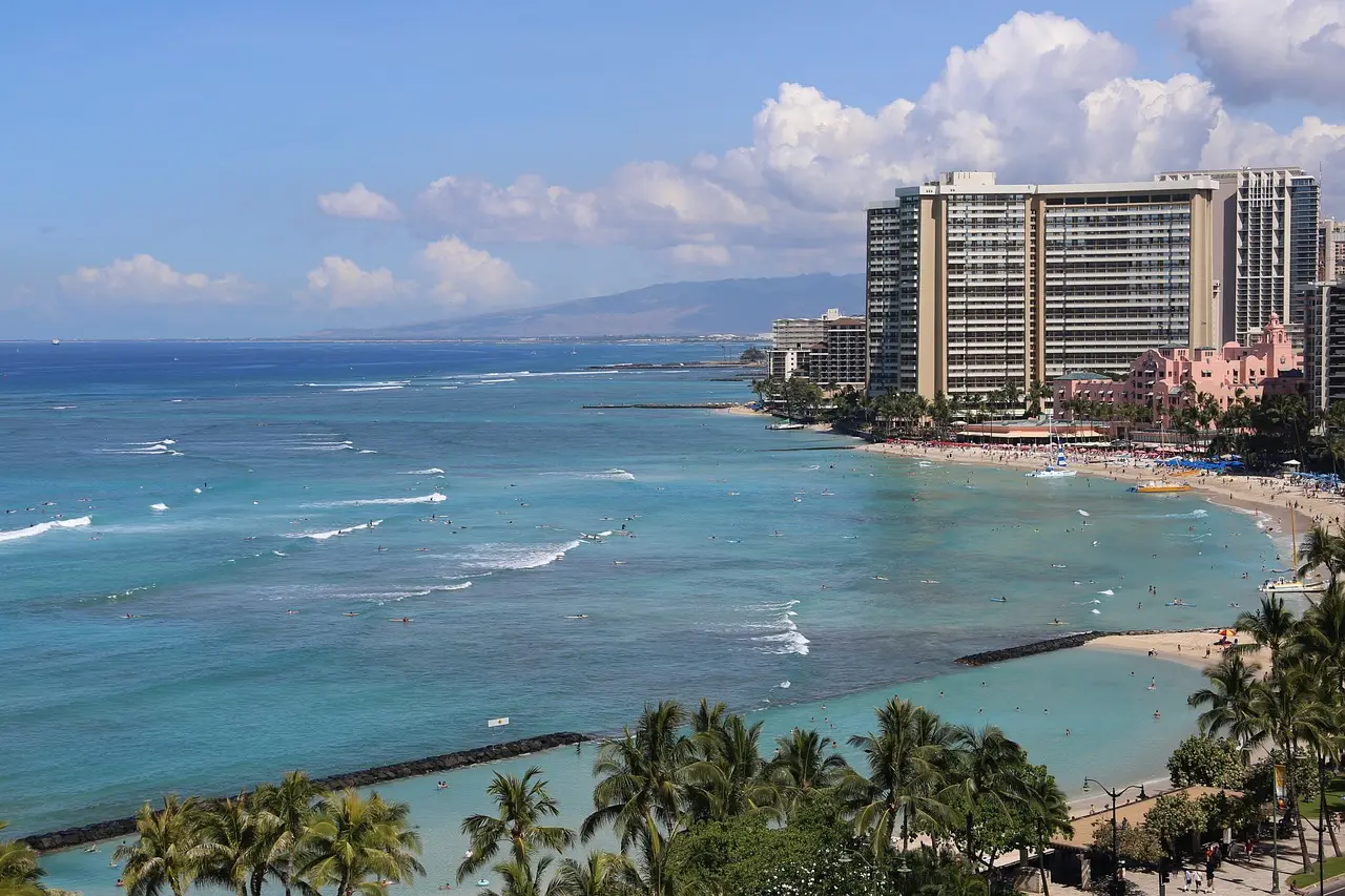 Playa de Waikiki en Oahu, Hawái, con oleaje suave, surfistas principiantes y palmeras alineadas bajo un cielo azul brillante Playa de arena blanca y aguas turquesa en Waikiki con surfistas y palmeras