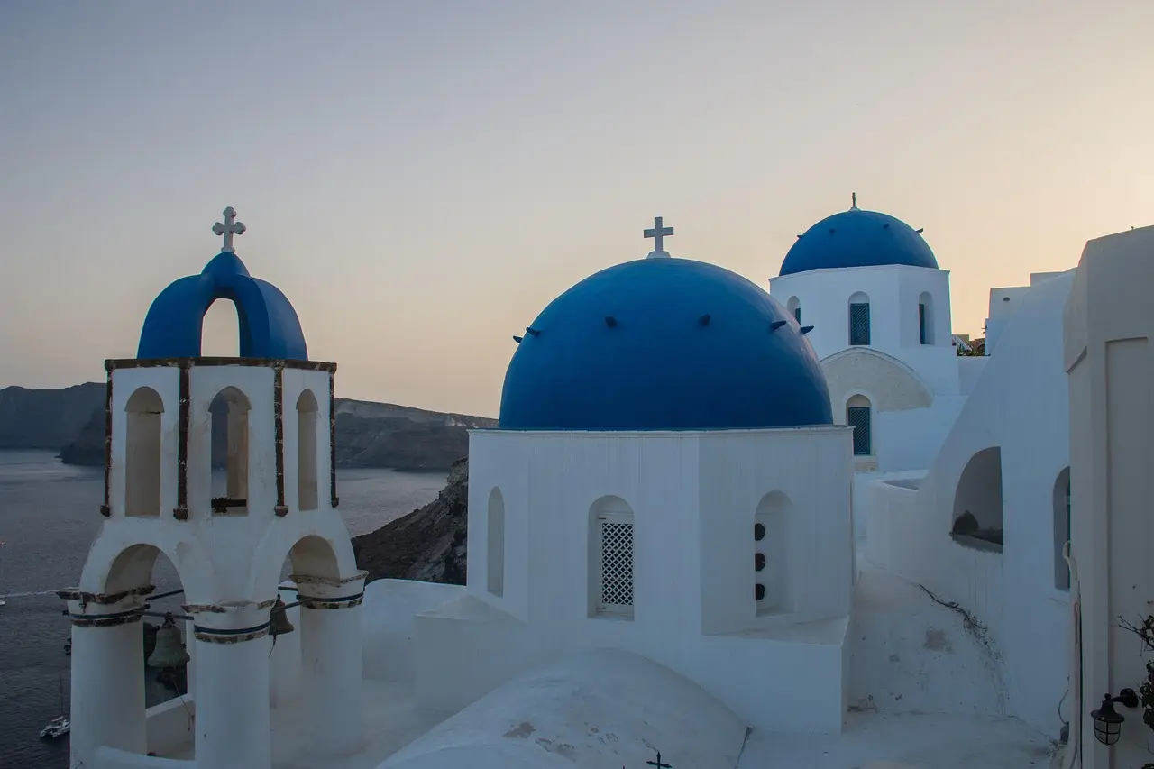 Romantic sunset in Oia, Santorini — a quintessential European honeymoon destination Sunset over whitewashed domes and blue roofs in Oia, Santorini, with cruise ships visible in the distance