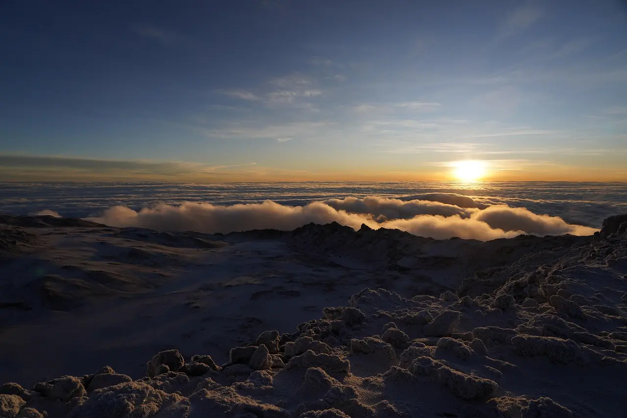 Solo climber reaching Uhuru Peak at dawn with snow-draped summit and expansive savanna stretching to the horizon Climber at Uhuru Peak on Mount Kilimanjaro at sunrise with snow cap and vast African plains below