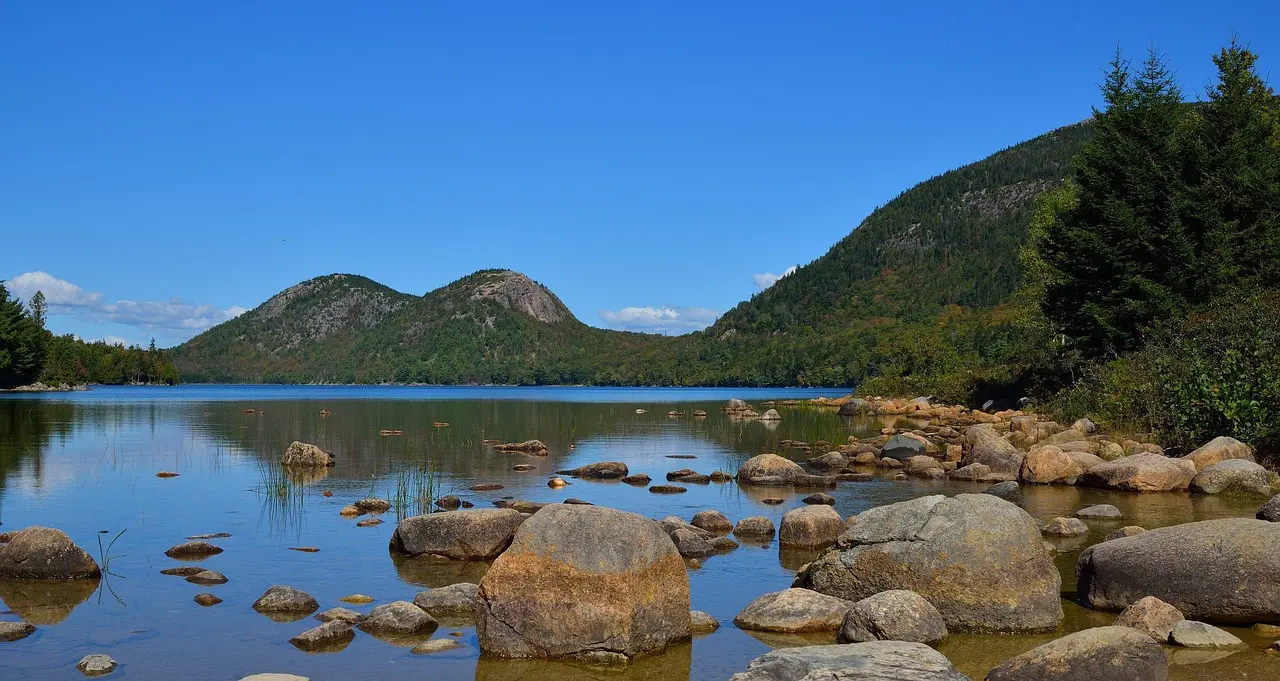 Costa rocosa del Parque Nacional de Acadia en Maine con olas intensas y árboles en colores otoñales rojos y dorados Acantilados rocosos de Acadia con olas rompiendo y bosque otoñal al fondo