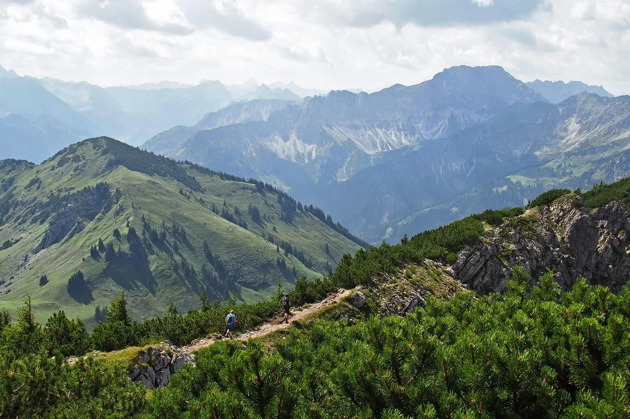 Scenic high-elevation hiking trail in the Alps with diverse terrain and panoramic views Aerial view of hikers on a winding mountain trail surrounded by pine forests and snow-capped peaks
