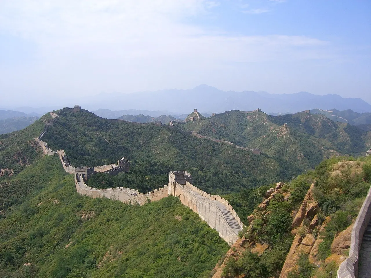 An aerial perspective reveals the Great Wall’s breathtaking scale as it winds through mist-shrouded peaks — a defining image of visiting ancient landmarks in Asia. Aerial view of the Great Wall snaking across mist-covered mountains in China