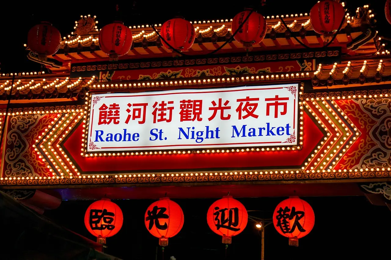 Raohe Night Market in Taipei: A warm, lantern-lit shopping destination for travelers craving flavor, craft, and connection Nighttime shot of Raohe Night Market with glowing red lanterns, steaming food carts, and crowds holding paper bags