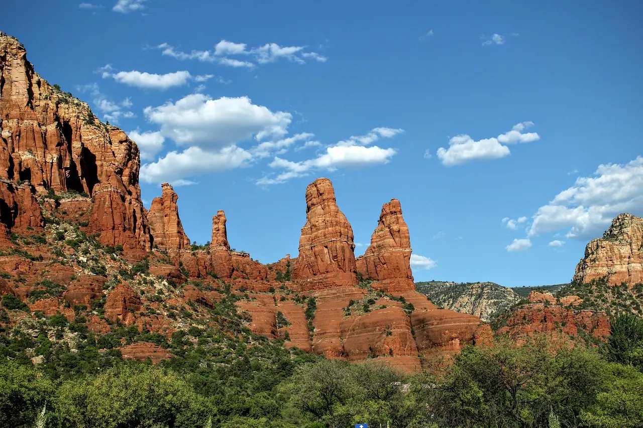 The geomagnetically active red rock formations of Sedona—creating a natural resonance field for deep relaxation travel. Red sandstone buttes at sunrise with soft shadows and sparse juniper trees, desert stillness