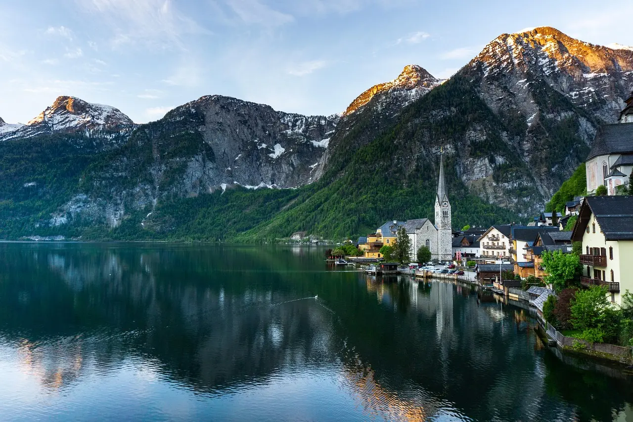 Aldea de Hallstatt reflejada en un lago alpino con montañas nevadas